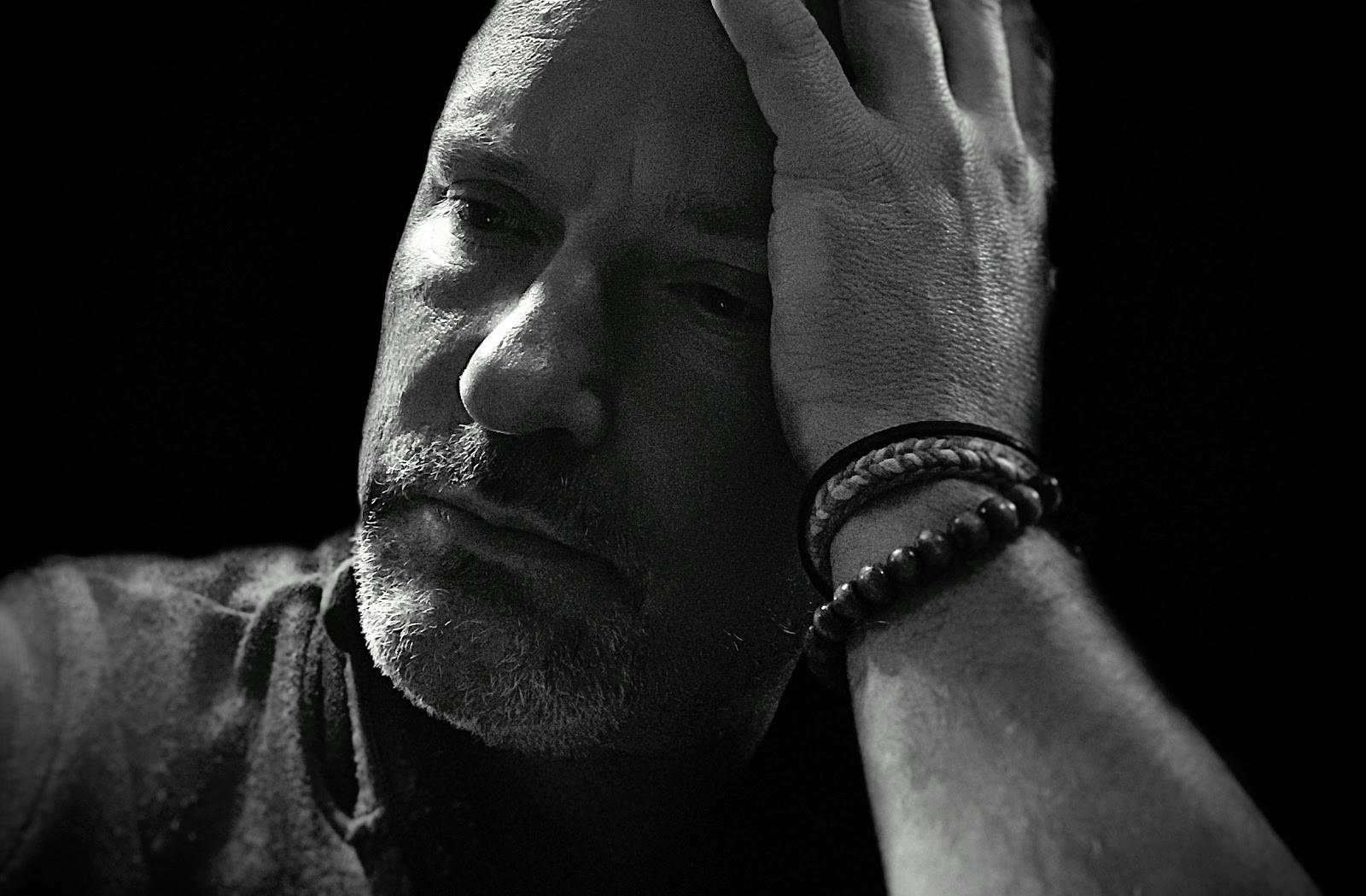 A black and white portrait of a man with his hand on his forehead, looking contemplative
