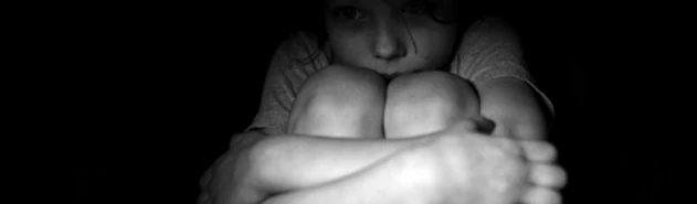 A child curled up in the darkness with arms wrapped around their knees