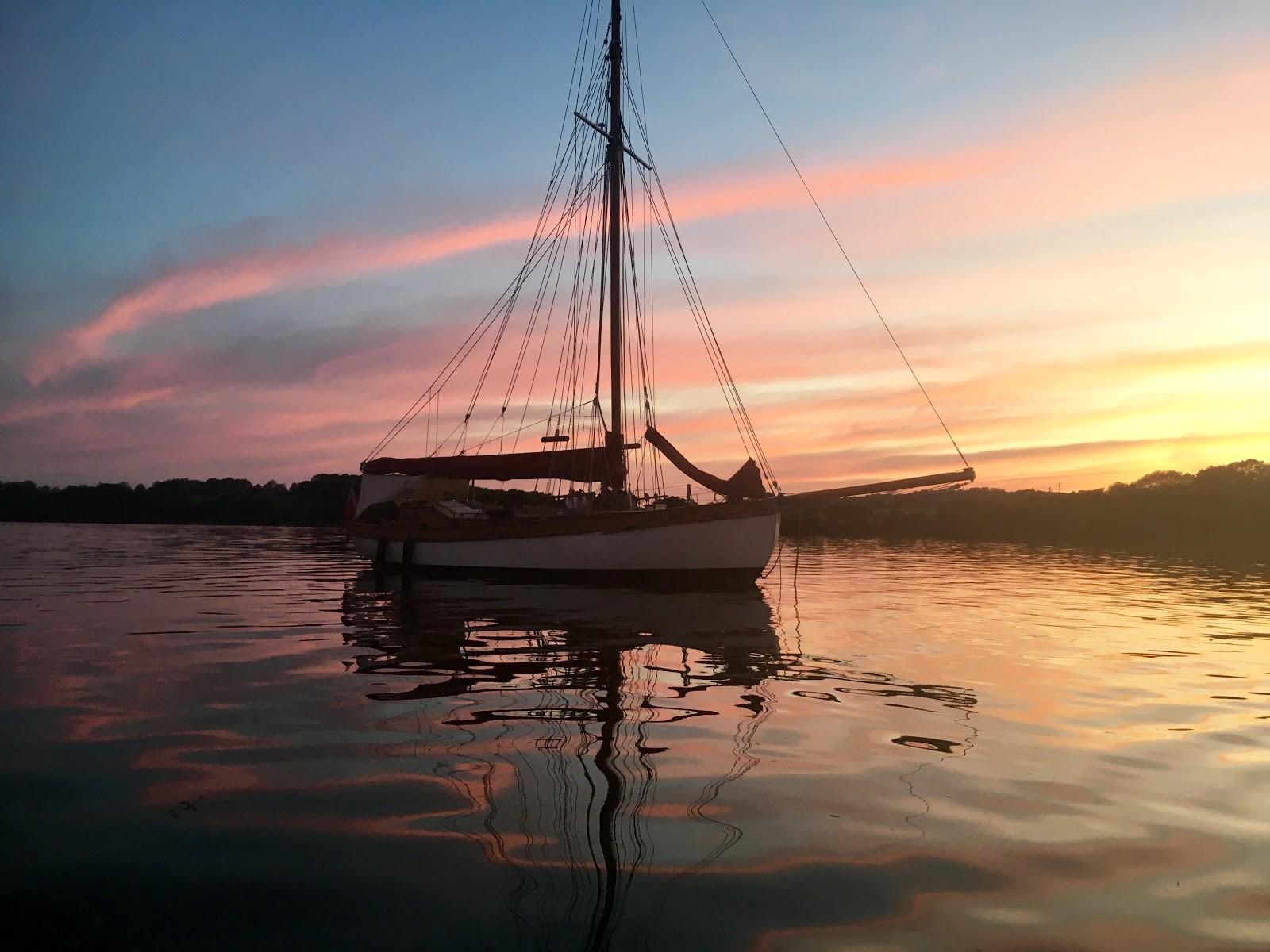 A wooden sailing yacht, Maid of Wyven, anchored on calm water at sunset