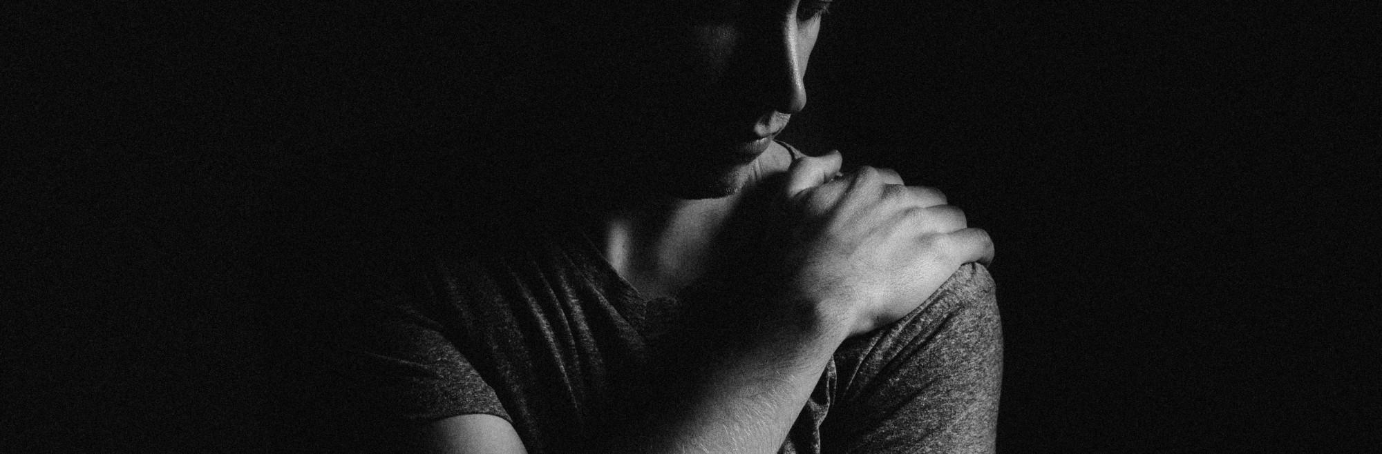 A person with their hand on their shoulder in shadow