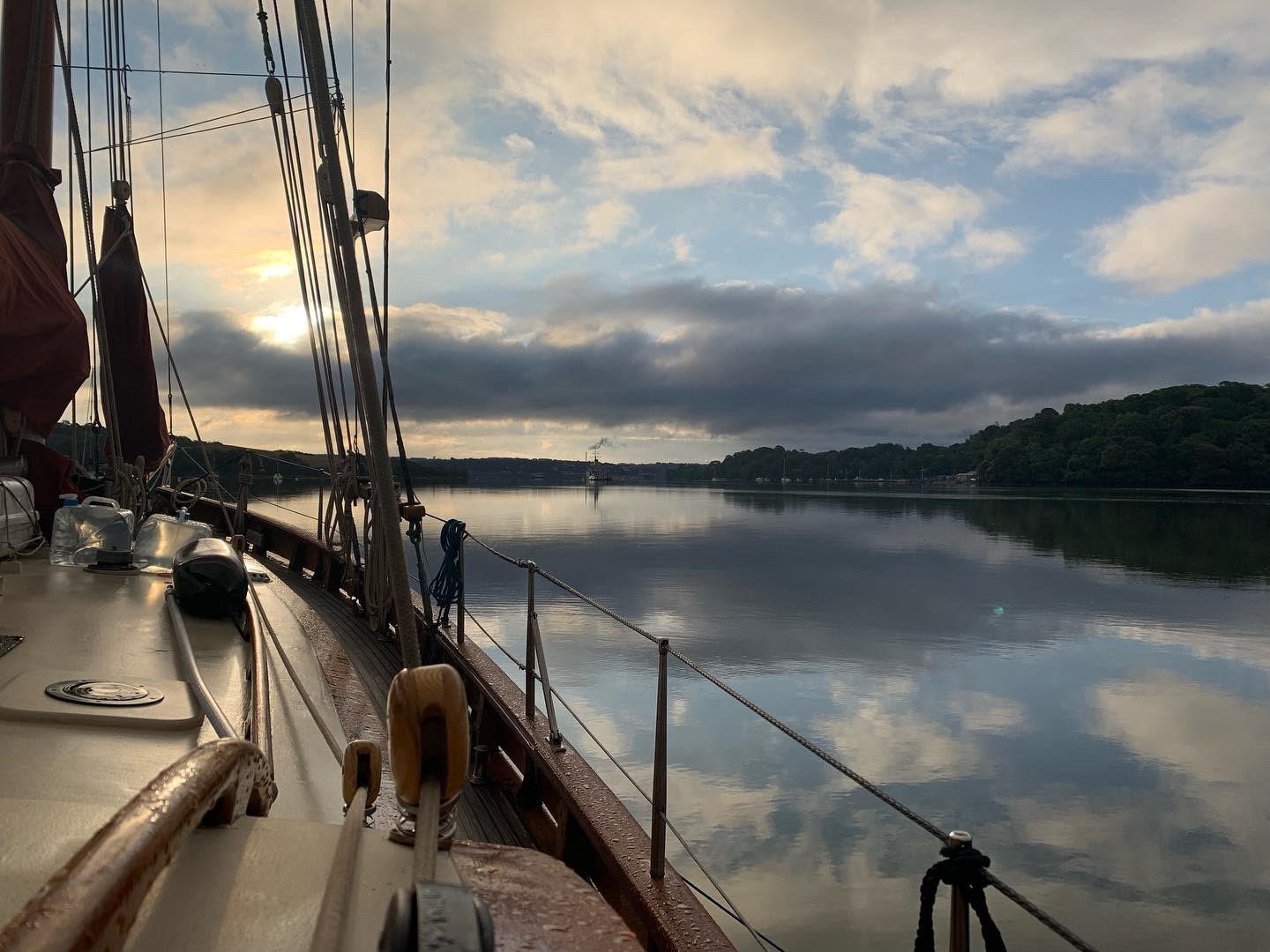 A view from the deck of a sailboat at anchor on a calm river at sunset